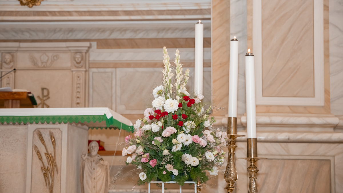 Fiori bianchi e rossi fra tre ceri accesi, sull’altare di marmo di una chiesa.
