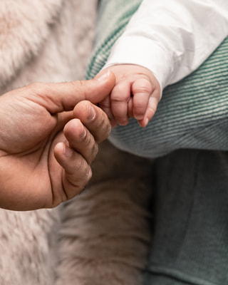 Una mano adulta tiene le dita di un neonato, tra una pelliccia chiara e la lana verde.