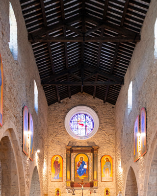 La navata di una chiesa in pietra con le panche vuote e il rosone in alto.
