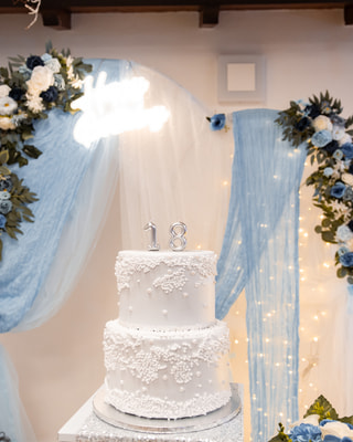 La torta a due piani con il «18» d’argento sotto un arco di fiori azzurri e bianchi, tulle e lucine, prima dell’arrivo degli ospiti.