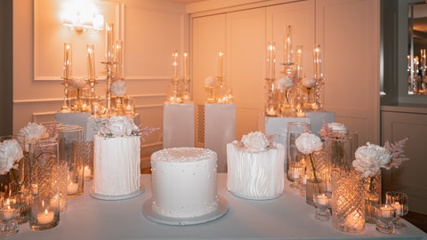 Il tavolo delle torte a lume di candela: tre torte bianche, peonie, cristalli e candele.