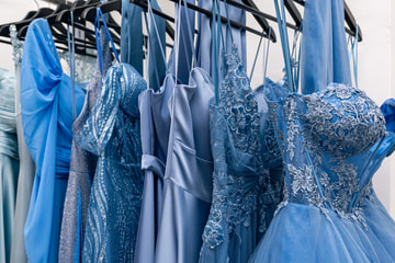 Abiti da cerimonia in tutte le sfumature dell’azzurro, di tulle, pizzo e raso, appesi a una stanga.