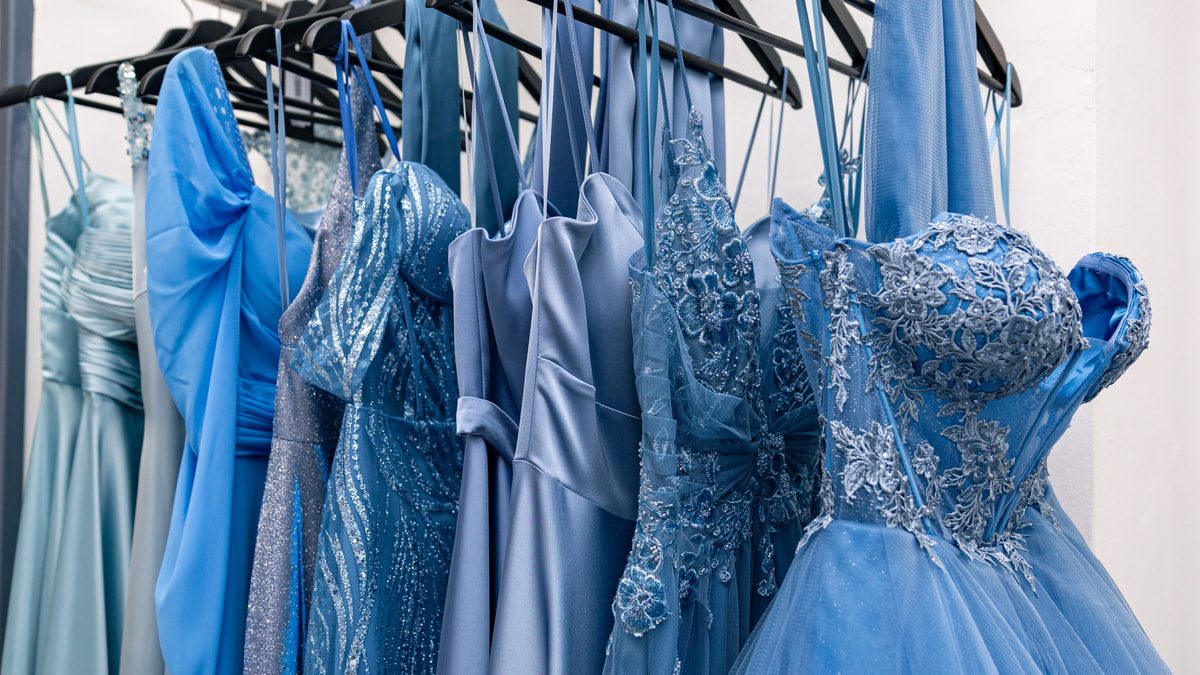 Abiti da sera in tutte le sfumature dell’azzurro, di tulle, pizzo e raso, appesi a una stanga.
