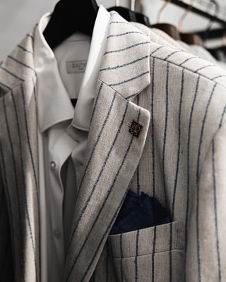 Una giacca gessata beige con il fazzoletto blu nel taschino, su una gruccia nera, ripresa da vicino.