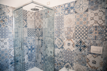 Un bagno con la doccia dal soffione a pioggia e le pareti di maioliche a disegni blu e bianchi, in luce chiara.