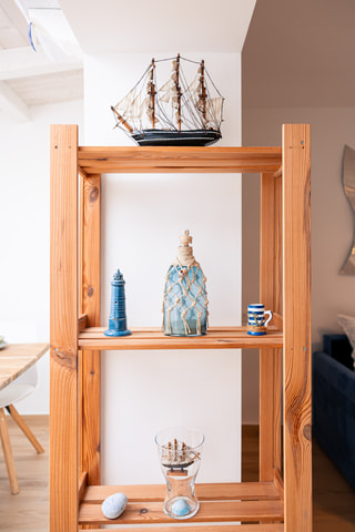 Uno scaffale di legno con un veliero, un faro, una bottiglia rivestita di corda e una tazza a righe.