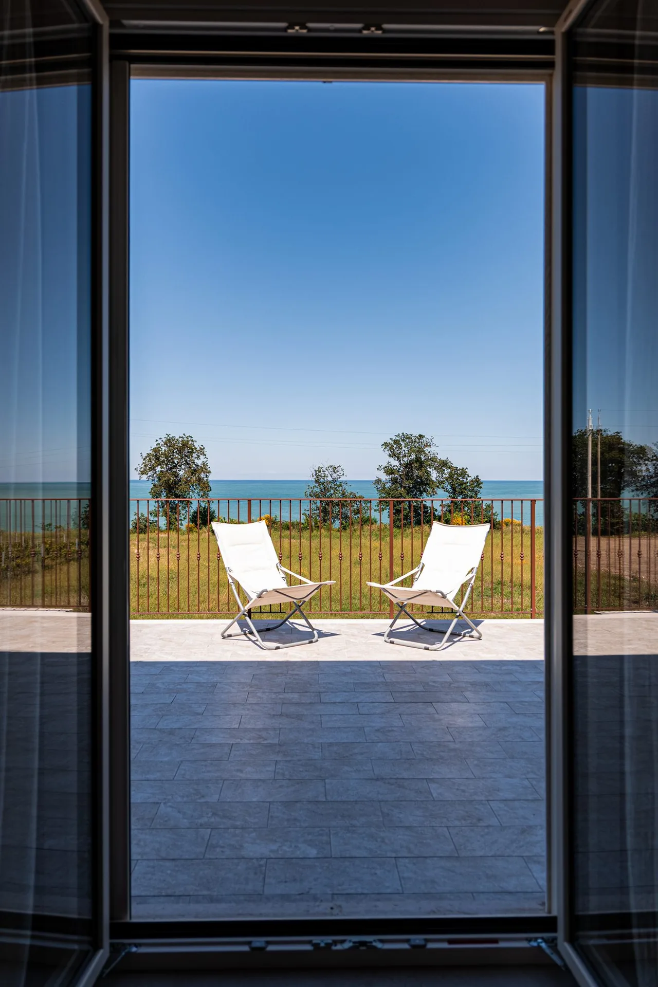Vista dalla vetrata su una terrazza con lettini e mare