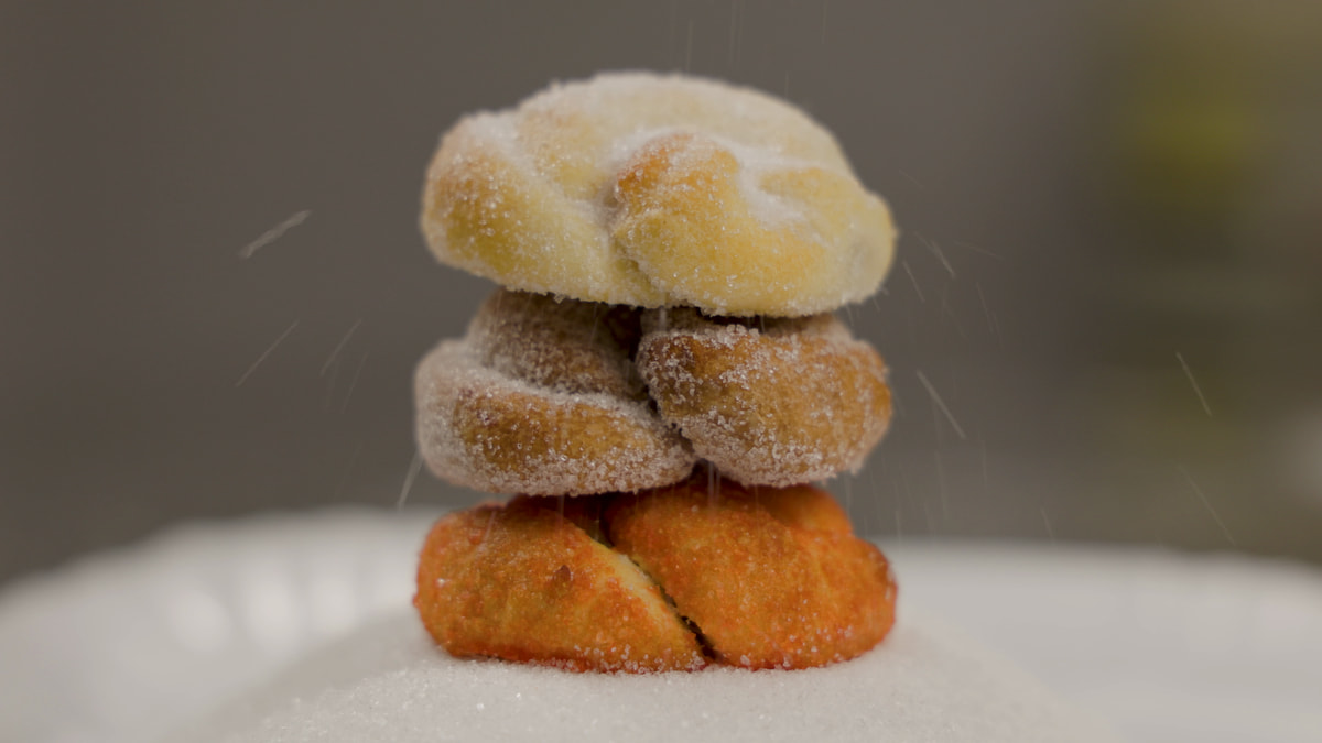 Tre dolci allo zucchero impilati su un piano coperto di zucchero, mentre lo zucchero cade piano dall’alto.