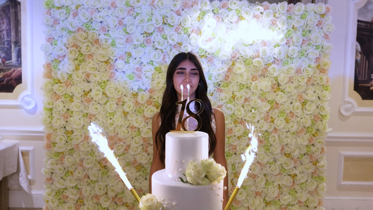 La festeggiata dietro la torta con il «18» e le candeline a stella, davanti a un muro di rose.